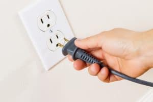 Horizontal photo of female hand inserting power cord receptacle into electric wall outlet